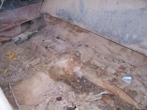 1955 Ford Customline - The interior of a car shows significant debris and a discarded bottle on the floor.