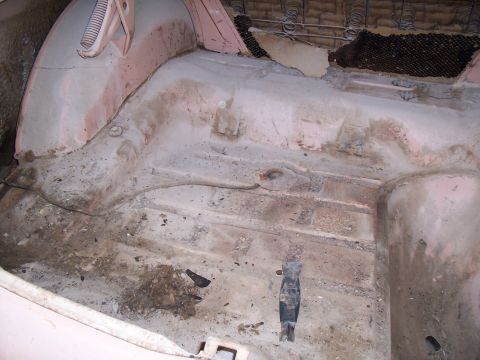 1955 Ford Customline - The interior floor of a car shows signs of wear and tear, with dirt and rust visible.