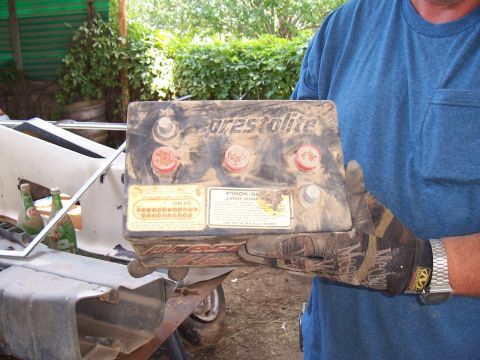 1955 Ford Customline - Dirty Prestolite car battery held by a person wearing work gloves.