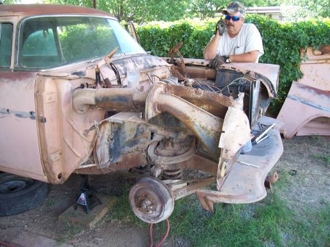 1955 Ford Customline - A faded pink 1950s Ford undergoing disassembly sits on a jack stand in a grassy yard, with the front clip, fenders, engine and inner struct…