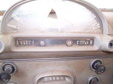 1955 Ford Customline - The interior of an older vehicle shows its dashboard gauges and controls, covered in dust.