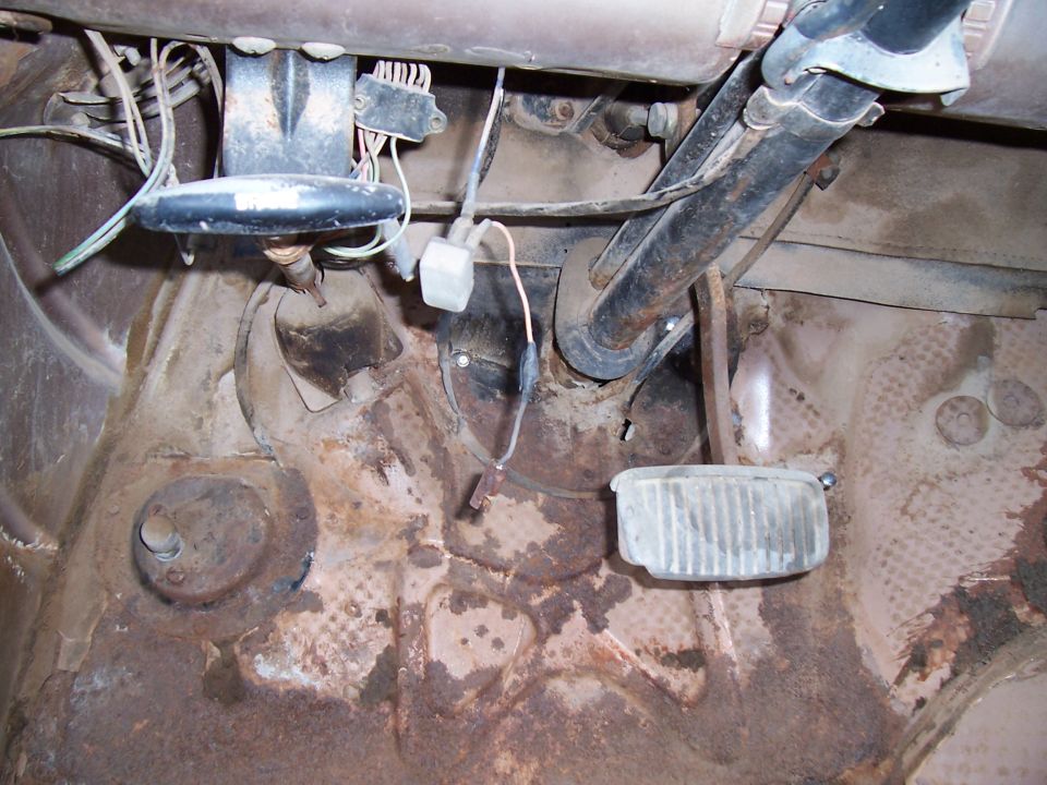 1955 Ford Customline interior floor pan showing brake and clutch pedals, steering column support, and wiring. Rust is visible