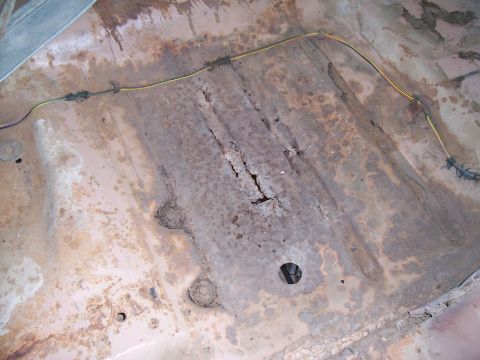 1955 Ford Customline - The interior floor of a car shows significant rust and damage.