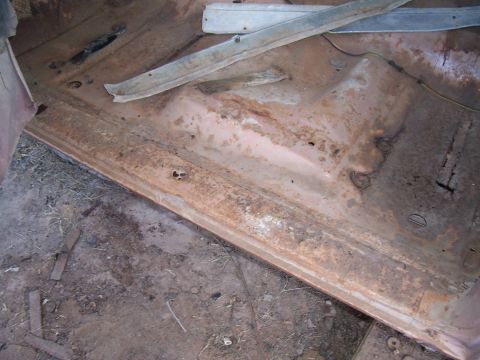 1955 Ford Customline - The interior floor pan of a 1955 Ford Customline exhibits significant rust and wear, indicating a need for restoration.