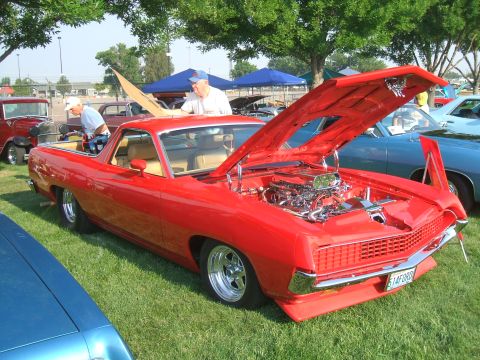 1974 Ford Ranchero - A red coupe utility, likely from the early 1970s, is displayed with its hood open, revealing a polished chrome engine. The vehicle is parke…