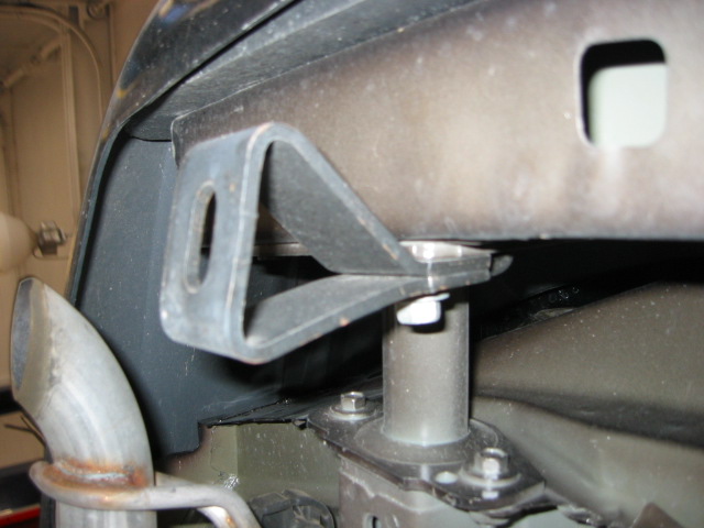 Underbody close-up of a steel bracket and cylindrical spacer on a car subframe