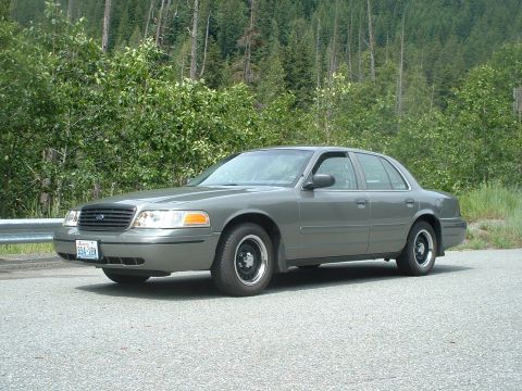 2000 Ford Crown Victoria - This 2000 Ford Crown Victoria is captured in a 3/4 front view, parked on the side of a road with a wooded background.
