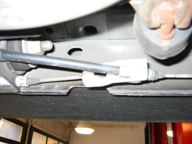 Vehicle underside showing brake lines, rubber hose, and metal fittings on gray frame