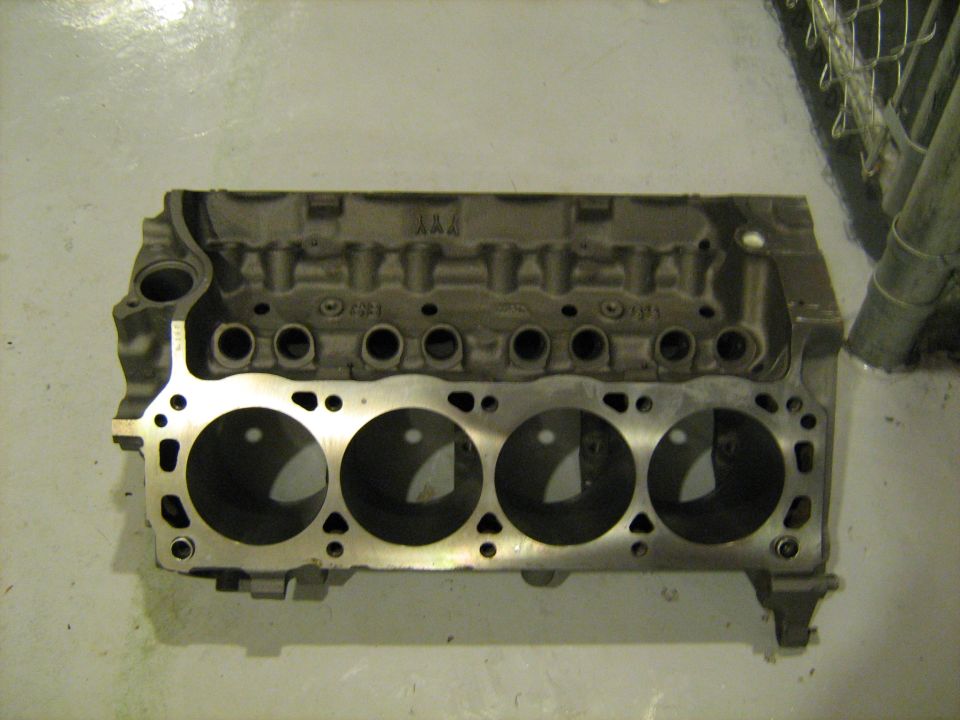 Engine block with four cylinders visible, metal casting, on a light-colored floor
