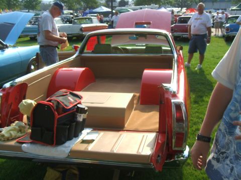 1974 Ford Ranchero - A red pickup truck is displayed at an outdoor event with other vehicles and attendees present.