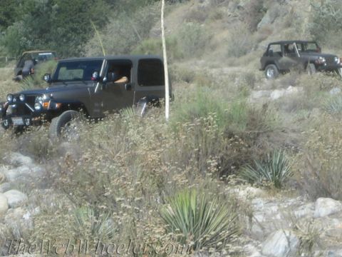 1987 Suzuki Samurai - Multiple Jeeps navigate a , dry, off-road trail with sparse vegetation.