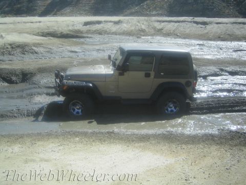 1987 Suzuki Samurai - A tan Jeep Wrangler navigates through a muddy terrain, its wheels partially submerged.
