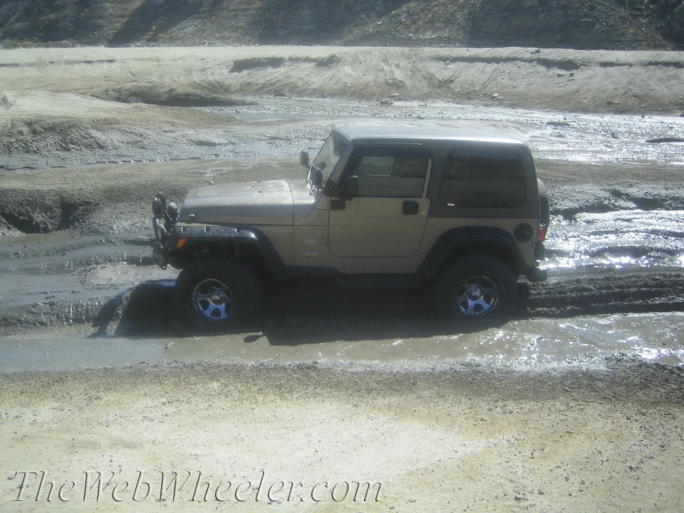 Tan Jeep Wrangler stuck in mud, side view, with aftermarket wheels and brush guard
