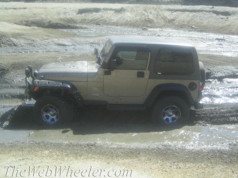 1987 Suzuki Samurai - A tan Jeep Wrangler navigates through a muddy terrain, with its tires partially submerged.