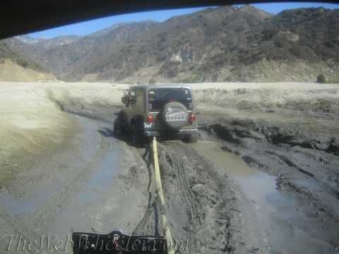 1987 Suzuki Samurai - Two vehicles navigating a muddy, off-road trail with mountains visible in the distance.