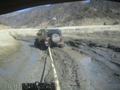 1987 Suzuki Samurai - A Jeep Wrangler is stuck in a muddy terrain, being assisted by another vehicle via a tow strap.