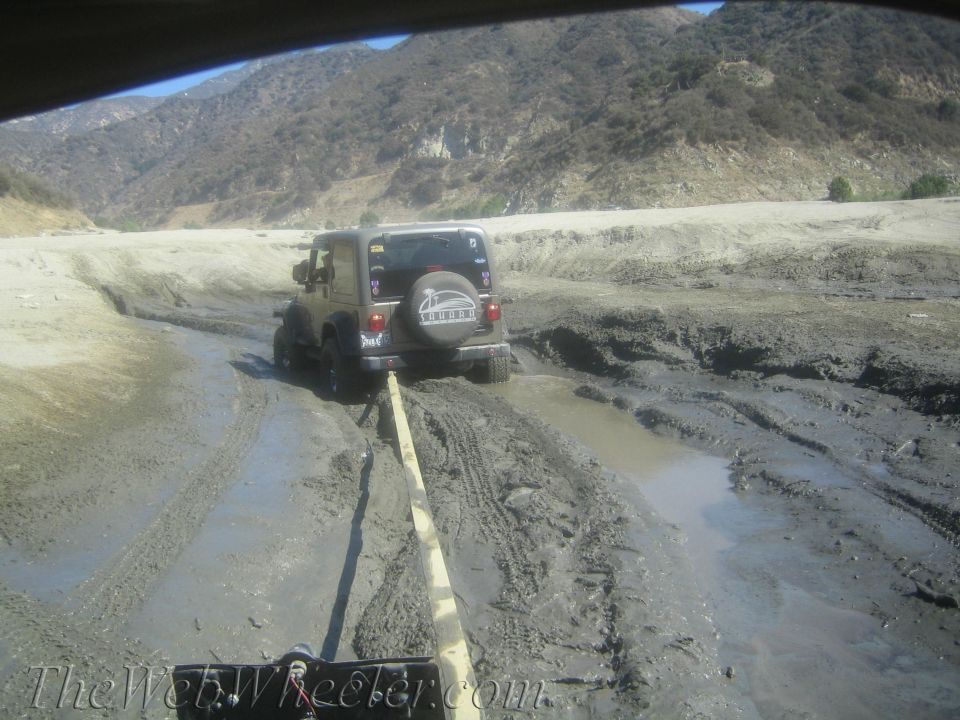 Jeep Wrangler being pulled out of mud with a tow strap. Mountains in background