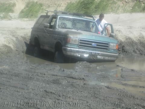 1987 Suzuki Samurai - A green Ford Bronco is stuck in thick mud with a person standing in the open driver's door.