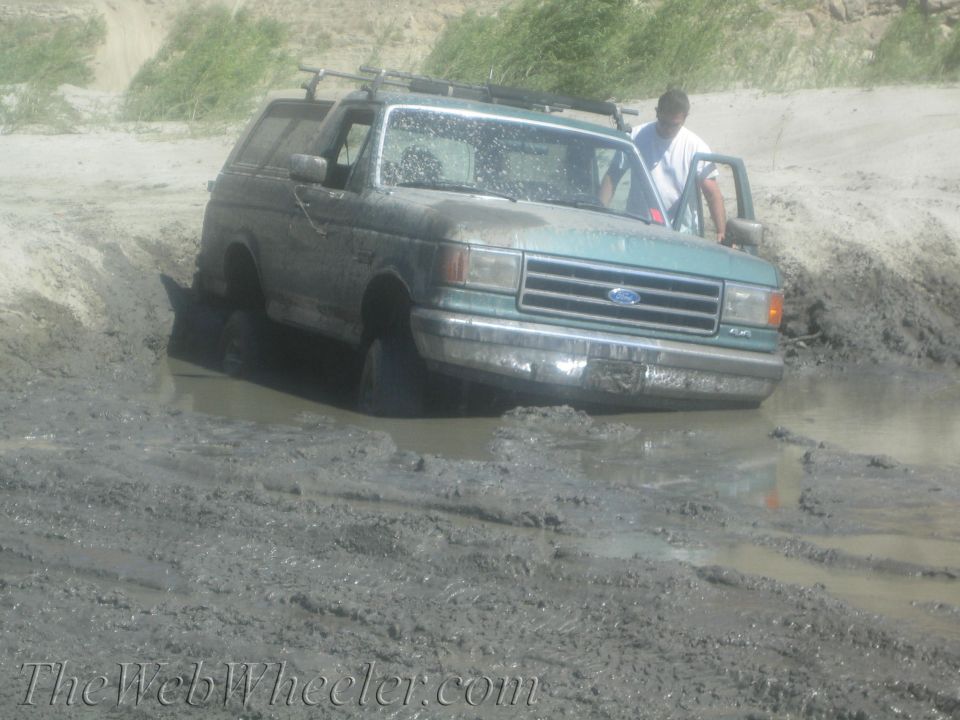 Green Ford Bronco stuck in mud, front view, driver's door open
