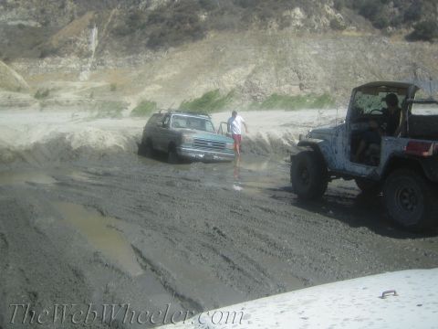 1987 Suzuki Samurai - A light blue Ford Bronco appears stuck in thick mud, while a Jeep is visible to the right.