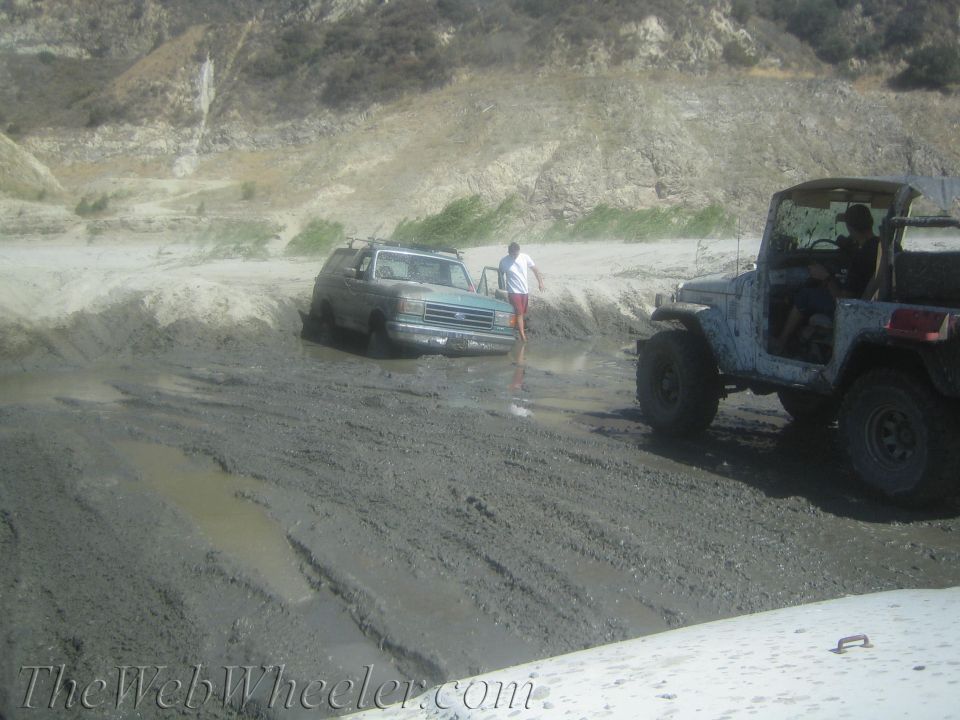 Light blue Ford Bronco stuck in mud, 1987 model year suggested by body style