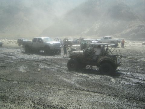 1987 Suzuki Samurai - Multiple vehicles are bogged down in a muddy terrain, with a dusty atmosphere obscuring the distant hills.