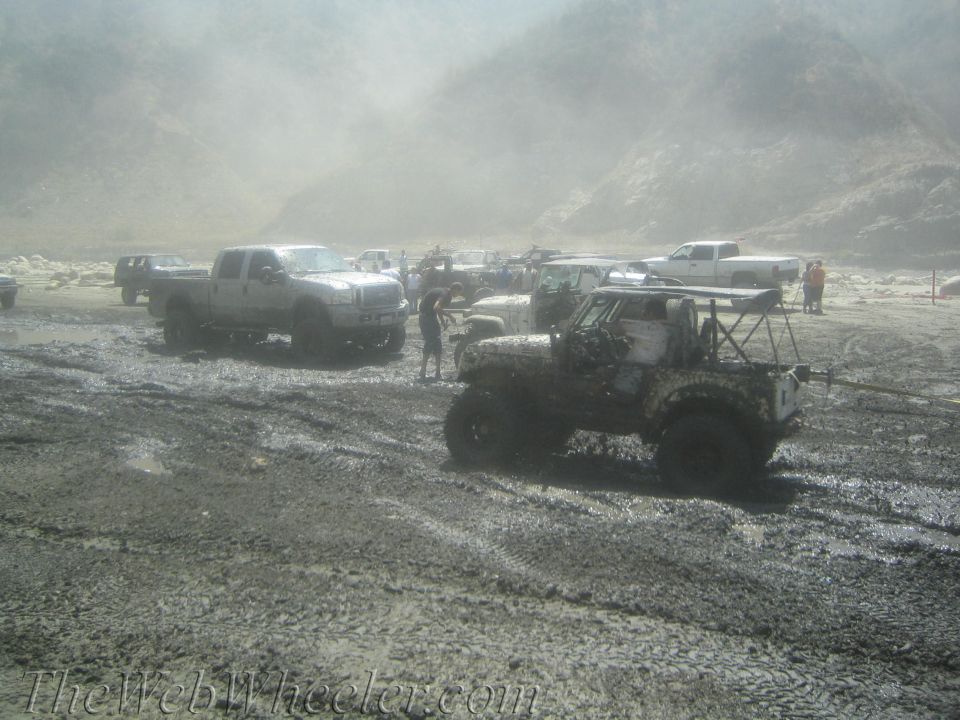 Several off-road trucks and jeeps stuck in thick mud with a dusty haze in the background
