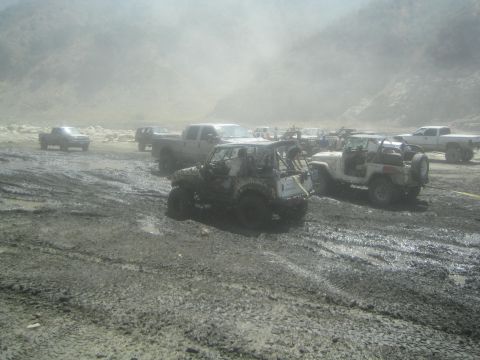 1987 Suzuki Samurai - Several off-road vehicles and trucks are parked in a muddy, dusty environment.