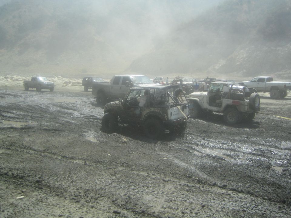 Mud-covered 1987 Suzuki Samurai parked in a muddy field with other off-road vehicles and trucks