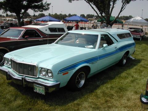 1972 Ford Ranchero - Light blue 1972 Ford Ranchero with blue stripes and a camper shell is displayed at a show.
