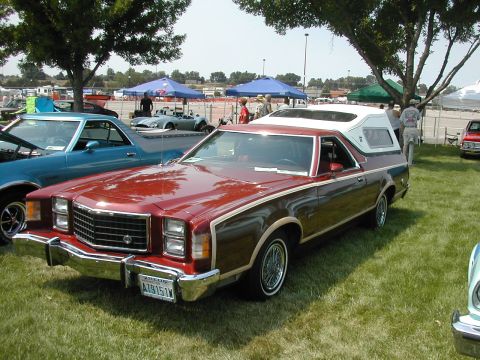 1972 Ford Ranchero - A red pickup truck with woodgrain trim and a white camper shell is parked on a grassy field at an outdoor event.