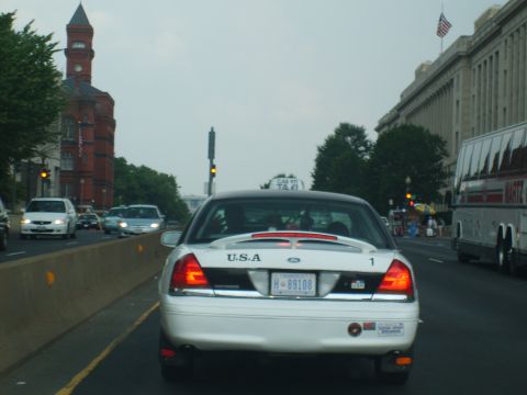 2004 Ford Crown Victoria - A white 2004 Ford Crown Victoria taxi drives on a city street, with other vehicles and buildings visible.