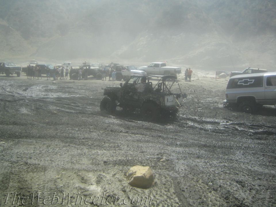 muddy off-road vehicles and people gathered in a dusty, hilly area