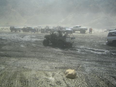 1987 Suzuki Samurai - Several off-road vehicles are parked in a muddy, dusty environment with hills in the background.
