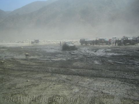 1987 Suzuki Samurai - Several off-road vehicles navigate a muddy terrain, with one SUV visibly stuck in the mire.