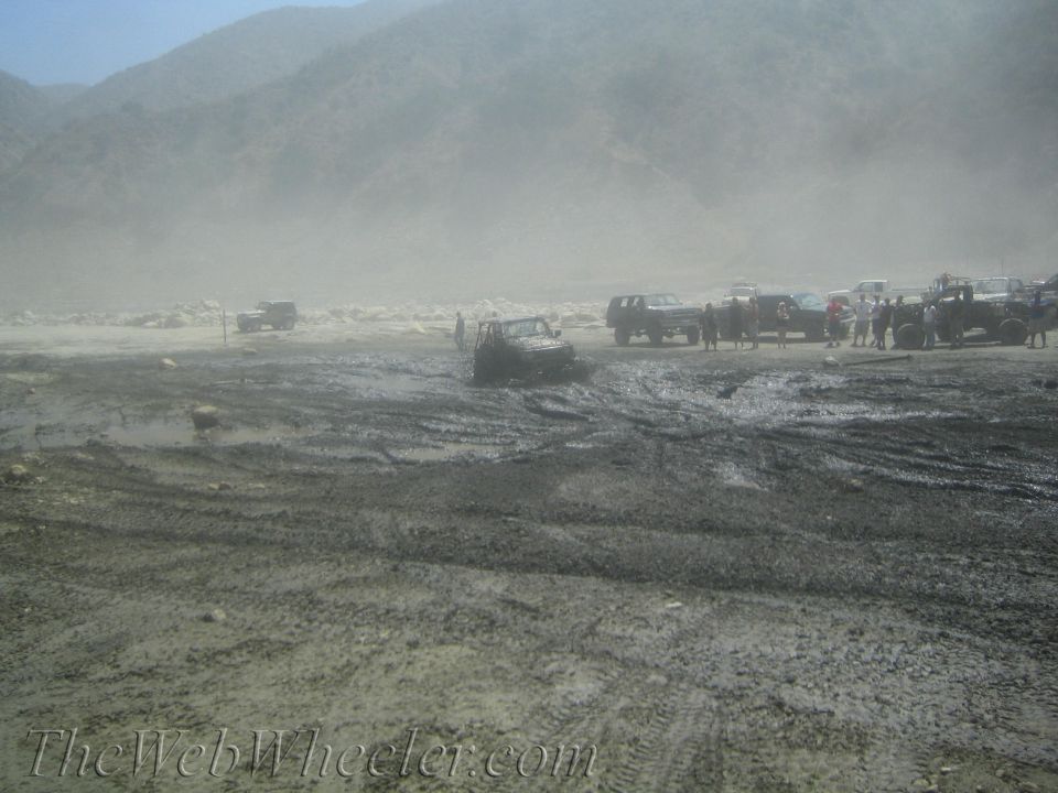 Muddy off-road scene with multiple SUVs and trucks, one stuck in mud