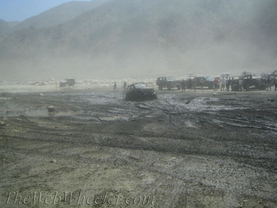 Several off-road vehicles stuck in thick mud with people standing around