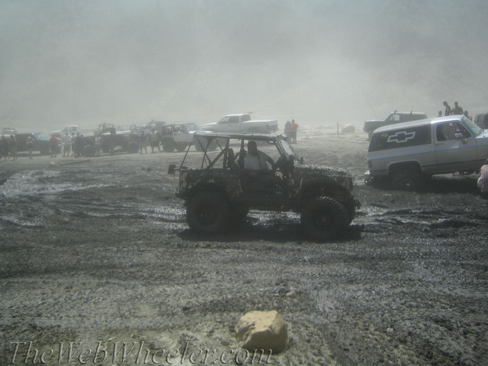 Muddy off-road vehicles gathered in a dusty, muddy area with people around