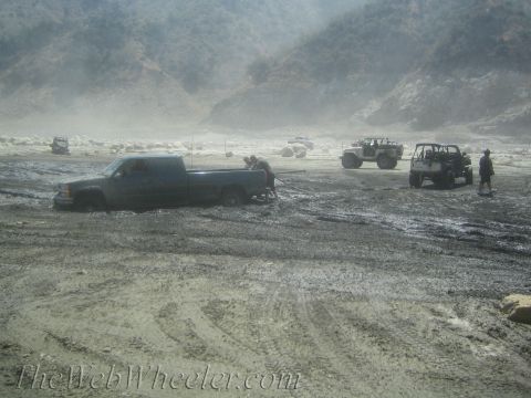 1987 Suzuki Samurai - Several off-road vehicles navigate a muddy terrain, with one pickup truck deeply stuck.