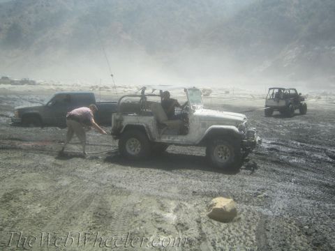1987 Suzuki Samurai - A white off-road vehicle is being towed through a muddy terrain by a pickup truck, with another off-road vehicle visible in the background.