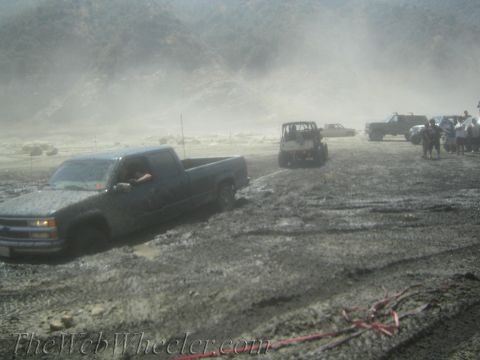 1987 Suzuki Samurai - Several off-road vehicles are navigating a muddy terrain, with one pickup truck appearing to be stuck.