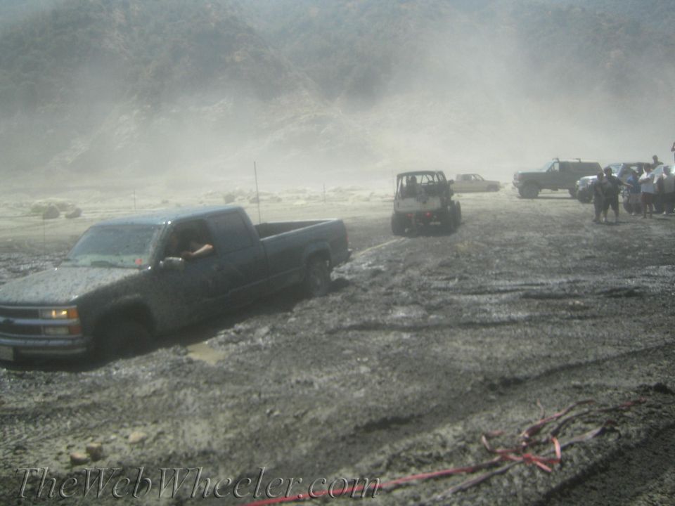 Pickup truck stuck in mud, with a jeep and other vehicles in the background