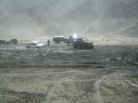 1987 Suzuki Samurai - Multiple off-road vehicles navigate a challenging muddy terrain, with one truck partially submerged.