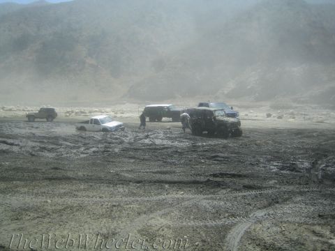 1987 Suzuki Samurai - Multiple off-road vehicles are mired in thick mud under a hazy sky, with a mountainous backdrop.