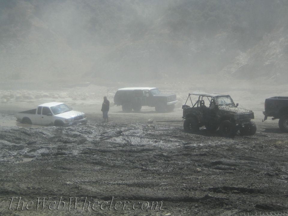 Several off-road vehicles stuck in thick mud, with dust or fog in the background