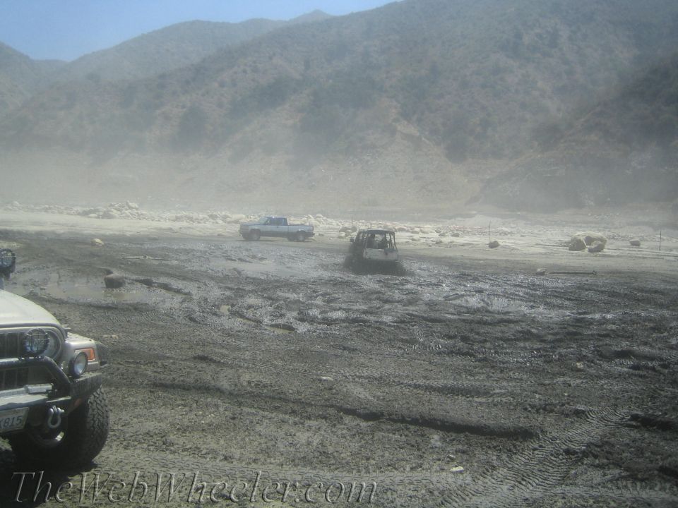 Muddy off-road vehicles in a dusty, mountainous terrain with a watermark