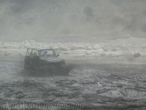 1987 Suzuki Samurai - A vehicle navigates a challenging muddy terrain, kicking up spray as it goes.