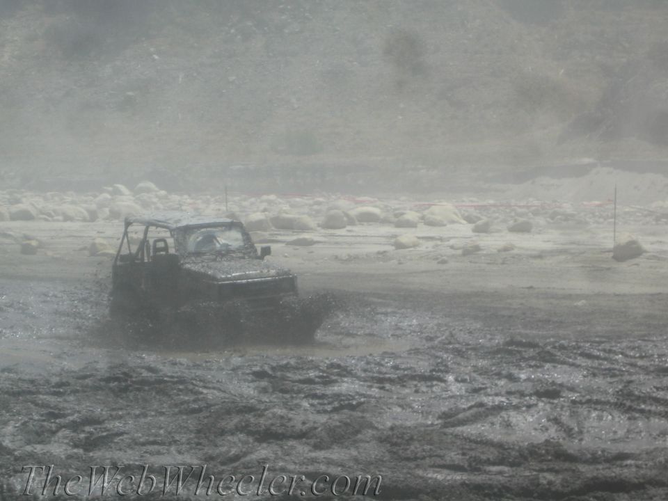 Jeep-like vehicle splashing through a muddy track with a dusty, rocky background