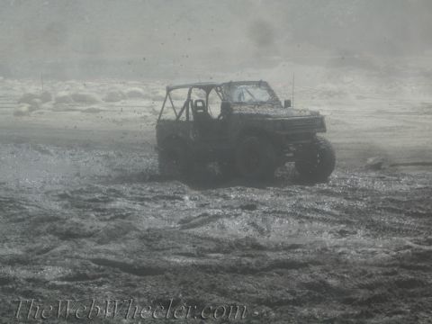 1987 Suzuki Samurai - Suzuki Samurai navigating a muddy terrain, with water and mud splashing around the vehicle.