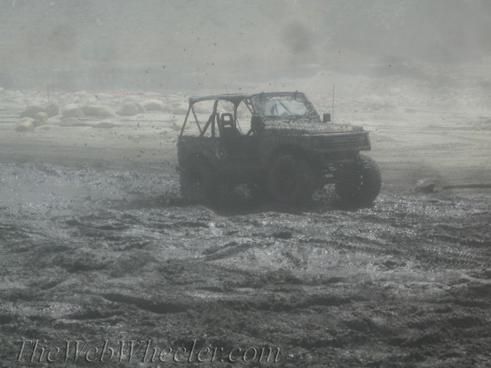 1987 Suzuki Samurai driving through deep mud, kicking up spray